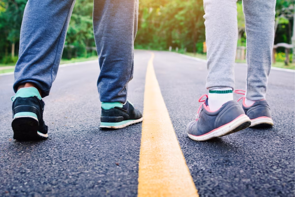 Duas pessoas caminhando no meio da rua. Um homem e uma mulher.