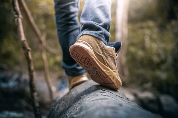 Pessoa caminhando em um tronco de árvore com um tênis beje e calça jeans.