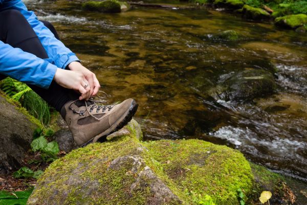 Pessoa amarrando os sapatos em um rio em cima das pedras.